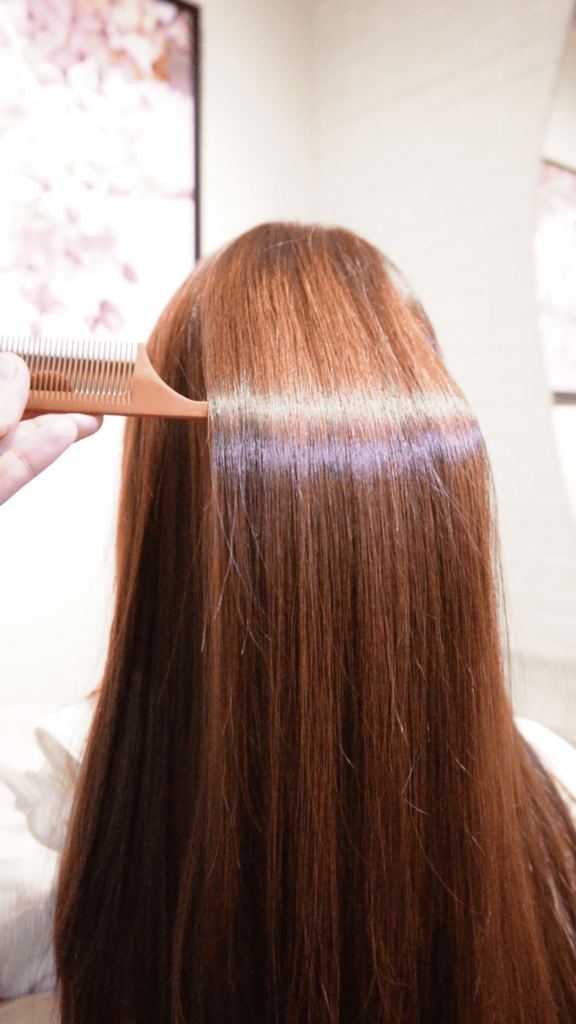 Stylist combing through healthy and shiny hair after a scalp treatment to prevent hair loss and thinning.