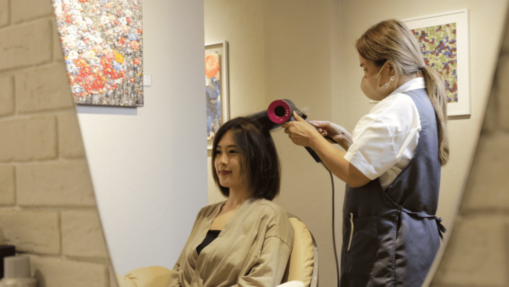 Therapist blowing hair for client and client smiling after a relaxing scalp treatment to reduce stress