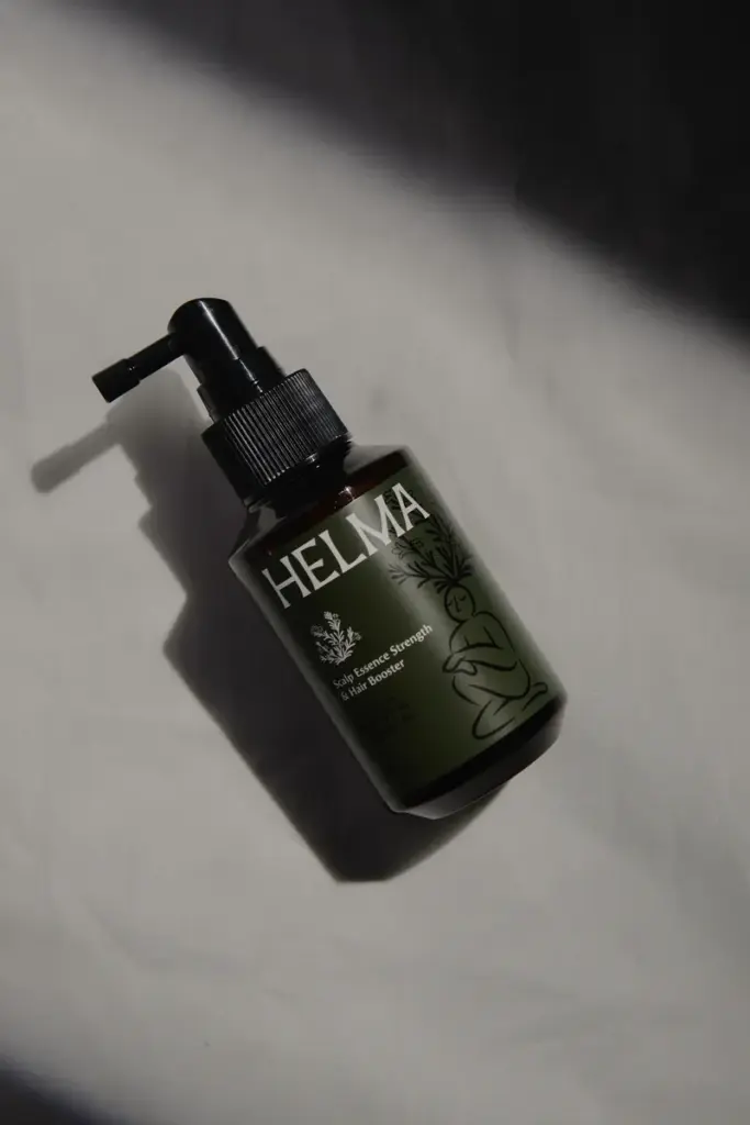 Helma scalp essence bottle placed on a light surface with natural shadow.