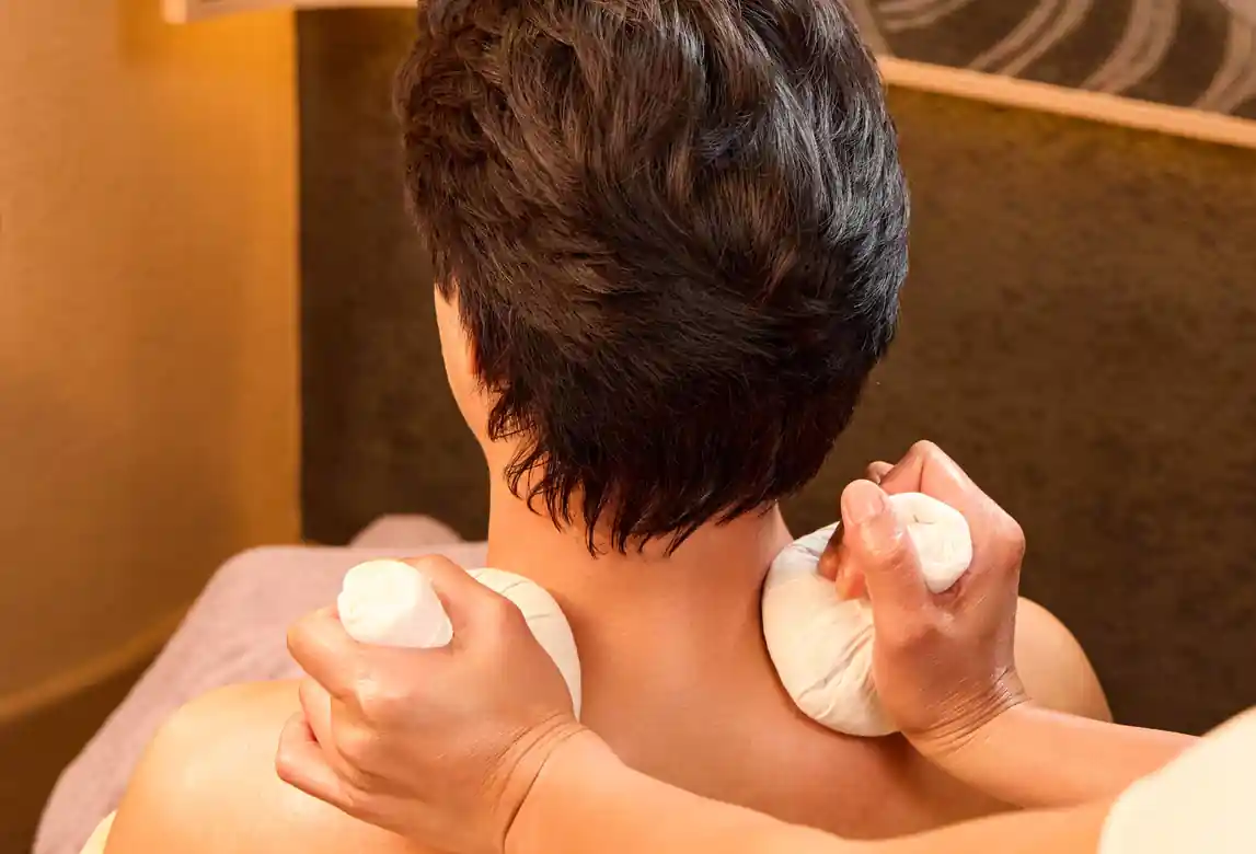 Therapist applying warm oil and herbal compress therapy to the neck and shoulders during the Aroma Oil Tranquility Program.