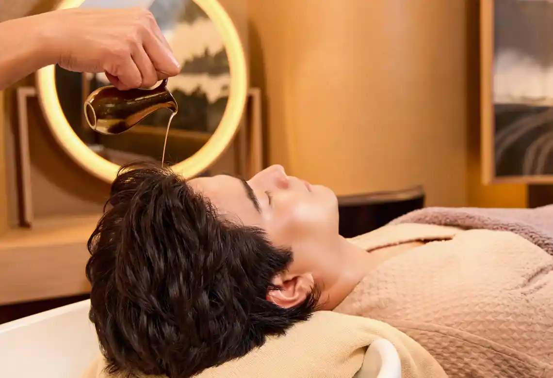 Therapist applying signature warm oil to the scalp and performing a soothing scalp and head massage during the Aroma Oil Tranquility Program.