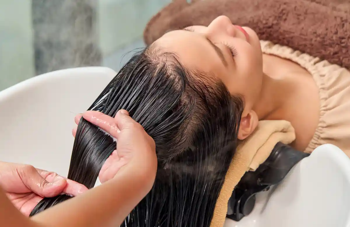 Therapist applying botanical nourishing hair treatment with bond-repair technology during the Signature Scalp program.